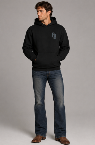 Man wearing a black hoodie with a logo and blue jeans on a gray background